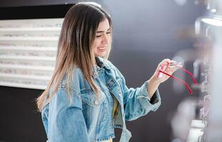 cliente la scelta bicchieri nel un occhiali negozio. bellissimo ragazza la scelta bicchieri nel un ottico negozio, giovane femmina acquirente la scelta bicchieri nel un ottico memorizzare foto