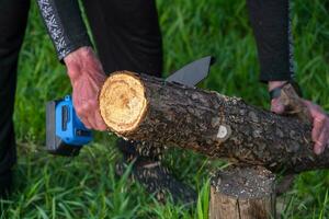 -Tenuto in mano portatile campeggio elettrico sega su un' batteria per taglio legna da ardere e Di legno. avvicinamento, un' mano segare un' tronco d'albero, schegge volante foto