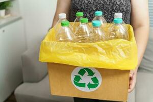 casa riciclare eco verde zero concetto donna lancio vuoto plastica bottiglia nel raccolta differenziata bidone con giallo spazzatura borse a casa. foto