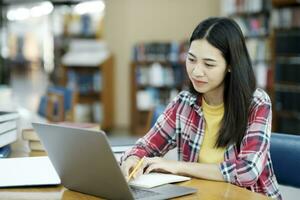 giovane Università alunno utilizzando il computer portatile per in linea apprendimento, ricerca e apprendimento a biblioteca. foto