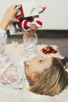 bambina carina sdraiata sul pavimento, che gioca con le decorazioni natalizie, il piccolo babbo natale che esce dalla scatola foto