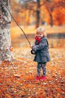 bella bambina che gioca a pescare con un ramo e un giocattolo di pesce, nel parco in una fredda giornata autunnale foto