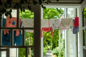 bambino Abiti sospeso su il stendibiancheria. bambini piccoli Abiti essiccazione su il balcone. corda con pulito bambini biancheria intima. casa interno foto