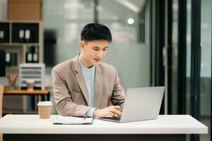 giovane asiatico attività commerciale uomo Lavorando a ufficio con computer portatile, tavoletta e assunzione Appunti su il carta. foto