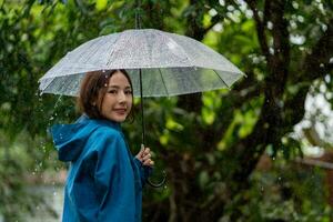 piovoso giorno asiatico donna indossare un' impermeabile all'aperto. lei è contento. foto