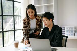 Due asiatico attività commerciale uomo e donna lavoratori parlando su il smartphone e utilizzando il computer portatile professionisti nel lavoro di squadra finanza, marketing, e successo foto