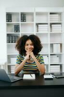 femmina studenti Nota a partire dal il libri a il africano ragazza biblioteca seduta a il scrivania utilizzando il computer portatile computer e tavoletta per ricerca un in linea informazioni. foto