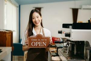 giovane femmina imprenditore sospeso un' benvenuto cartello nel davanti di un' caffè negozio. bellissimo cameriera o hostess Tenere un' tavoletta preparazione foto