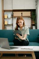 femmina studenti Nota a partire dal il libri a il asiatico ragazza biblioteca seduta a divano utilizzando il computer portatile computer e tavoletta per ricerca un in linea informazioni. foto