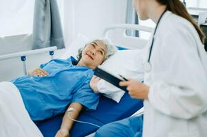 femmina anziano medico Tenere maschio paziente mano su il letto con ricevente soluzione salina soluzione nel ospedale foto