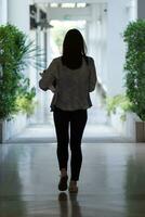 femmina internazionale scuola alunno vestito nel jeans camminava dentro scuola edificio su corridoio nel davanti di aula solo. indietro di femmina alunno chi era a piedi solo nel corridoio di scuola costruzione. foto