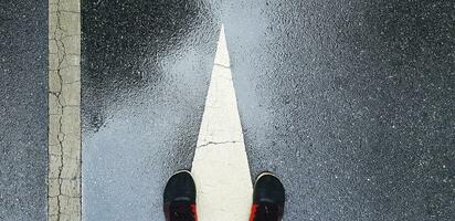 superiore Visualizza o piatto posare di sneaker o in esecuzione scarpe su bagnato strada o strada con bianca fine di direzione cartello e linea con copia spazio. scherzando e esercizio dopo pioggia. foto