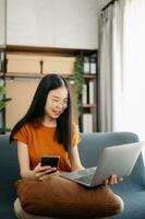 femmina studenti Nota a partire dal il libri a il asiatico ragazza biblioteca seduta a il divano utilizzando il computer portatile computer e tavoletta per ricerca un in linea informazioni. foto