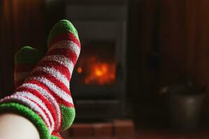 piedi gambe nel inverno Abiti lana calzini a camino sfondo. donna seduta a casa su inverno o autunno sera rilassante e riscaldamento su. inverno e freddo tempo metereologico concetto. hygge Natale vigilia. foto