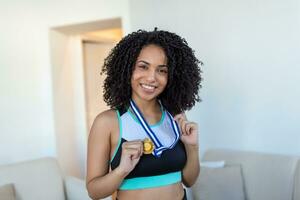 ritratto di un attraente giovane femmina atleta in posa con sua oro medaglia. africano americano atleta mostrando primo posto medaglia foto