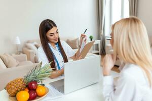 medico nutrizionista, dietista e femmina paziente su consultazione nel il ufficio. giovane sorridente femmina dietologo nel il consultazione camera. dietologo scrivania con salutare frutta e misurazione nastro. foto