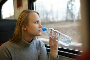 donna che beve acqua e guardando fuori dal finestrino del treno foto