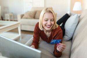 giovane donna su divano shopping in linea con addebito carta. bellissimo ragazza utilizzando il computer portatile computer per in linea shopping a casa foto