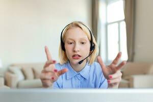 sorridente giovane donna utilizzando il computer portatile a casa, guardare a schermo, chattare, indossare senza fili cuffia avendo video conferenza . attività commerciale allenatore tutoraggio di webcam, in linea addestramento, e-coaching concetto foto