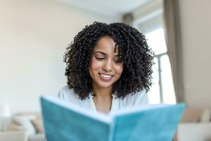 giovane bellissimo africano americano donna Tenere prenotare, Università alunno studiando, apprendimento linguaggio. tempo libero, letteratura e persone concetto - sorridente africano americano donna lettura libro a casa foto