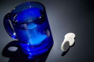 tavoletta dissoluzione nel un' blu bicchiere di acqua. foto