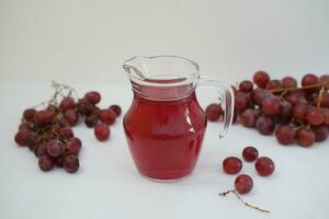 uva succo nel un' bicchiere brocca con fresco uva su un' bianca sfondo foto