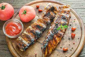 costolette di maiale alla griglia con pomodori sulla tavola di legno foto