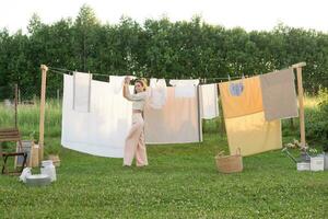 lavanderia giorno. un' donna si blocca biancheria e asciugamani su un' albero nel il cortile di un' villaggio Casa. foto