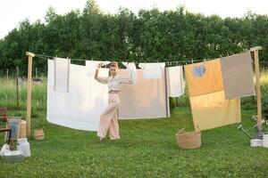lavanderia giorno. un' donna si blocca biancheria e asciugamani su un' albero nel il cortile di un' villaggio Casa. foto