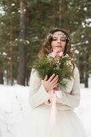 bellissimo sposa nel un' bianca vestito con un' mazzo nel un' innevato inverno foresta. ritratto di il sposa nel natura foto