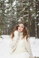 bellissimo sposa nel un' bianca vestito con un' mazzo nel un' innevato inverno foresta. ritratto di il sposa nel natura. foto