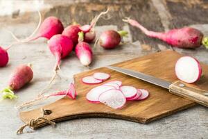 fresco tritato Ravanelli e un' coltello su un' taglio tavola su un' di legno tavolo. verdure per un' vegetariano dieta. rustico stile foto