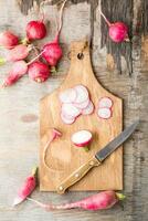 fresco tritato Ravanelli e un' coltello su un' taglio tavola su un' di legno tavolo. verdure per un' vegetariano dieta. rustico stile. verticale e superiore Visualizza foto