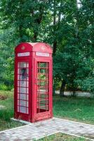 vecchio Vintage ▾ rosso telefono pubblico cabina su il marciapiede nel il strada. antiquato comunicazioni foto