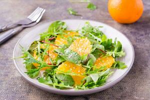 dieta vegetariano vitamina insalata di arancia pezzi e mescolare di rucola, bietola e mizun le foglie su un' piatto su il tavolo. avvicinamento foto