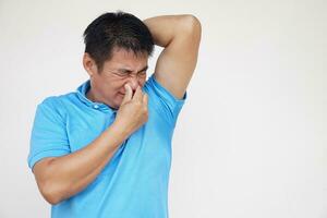 asiatico uomo è controllo il suo odore ascelle, vicino il suo naso con mano, sentire disgustato il corpo forte odore. concetto , Salute problema. sgradevole corpo odore , odore cattiva reazione. negativo emozione. foto