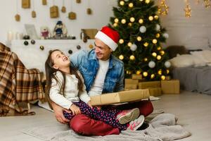 ritratto di un' sorpreso poco ragazza con sua padre Tenere un' Natale presente foto