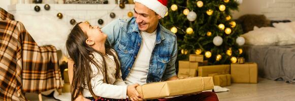 ritratto di un' sorpreso poco ragazza con sua padre Tenere un' Natale presente foto