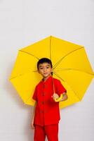 poco ragazzo moda un' sorridente bambino Tenere un' giallo ombrello nel un' rosso Cinese vestire. Cinese nuovo anno, Cinese nuovo anno foto