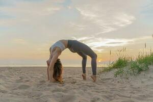 femmina fitness allenatore su il sabbia spiaggia tramonto sfondo. meditazione e armonia e equilibrio di un' persona, mentale Salute. praticante yoga esercizi asana. foto