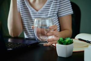 donna detiene bicchiere di acqua mentre lavori a casa posto di lavoro foto