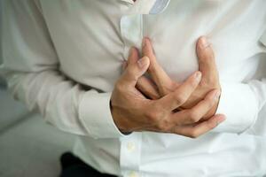 mano hold il petto con cuore attacco sintomi, asiatico uomo Lavorando difficile avere il petto dolore causato di cuore patologia, perdere, dilatazione, allargata coronario cuore, stampa su il il petto con un' doloroso espressione foto