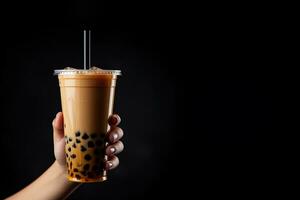 un' mano Tenere porta via plastica tazza di delizioso ghiacciato bolla latte tè e nero perle isolato su nero sfondo con copia spazio. ai generato foto