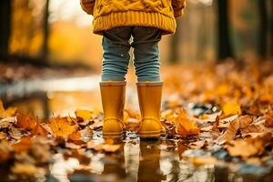 bambino in piedi su fogliame gambe nel stivali in piedi nel autunno pozzanghera con arancia le foglie foto