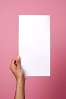 un' umano mano Tenere un' vuoto foglio di bianca carta o carta isolato su rosa sfondo. ai generato foto