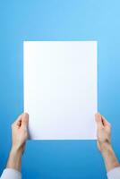 un' umano mano Tenere un' vuoto foglio di bianca carta o carta isolato su blu sfondo. ai generato foto