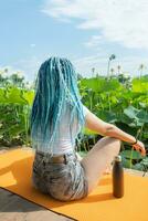 giovane donna con bellissimo blu dreadlocks riposo su yoga stuoia su loto lago foto