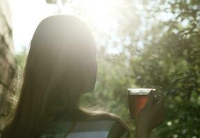 donna con tazza di tè nel sera luce del sole foto