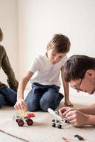 padre e ragazzi si divertono a costruire auto robot a casa seduti sul tappeto foto