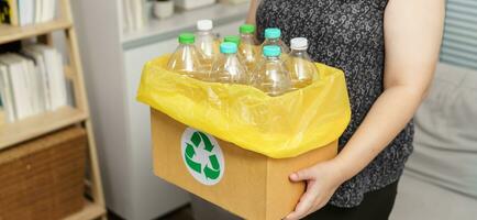 casa riciclare eco verde zero concetto donna lancio vuoto plastica bottiglia nel raccolta differenziata bidone con giallo spazzatura borse a casa. foto